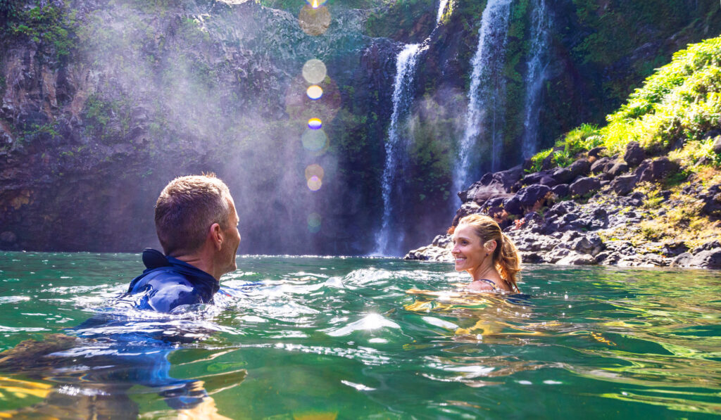 Couple swimming in an emerald plunge pool below twin waterfalls on a private Big Island waterfall hike-and-swim tour