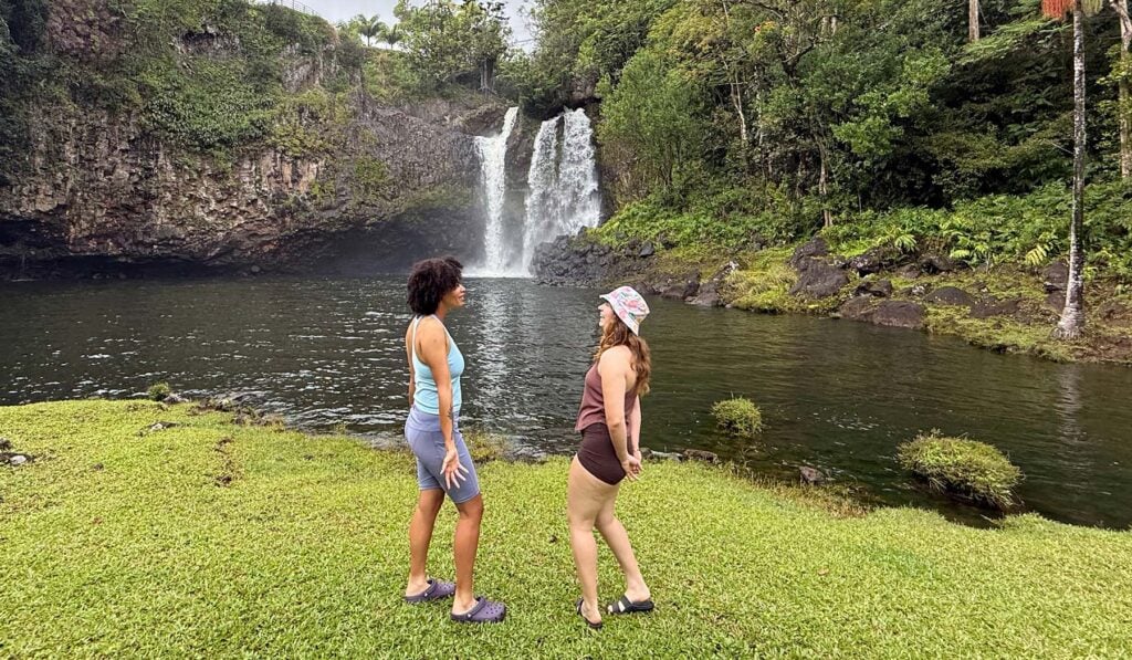Two hikers in water shoes standing at the edge of a calm waterfall pool before entering the water